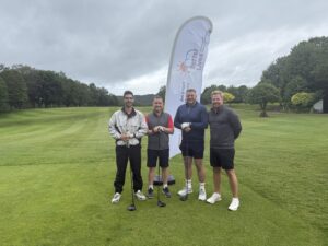 Image of four men on a golf course stood in front of a flag