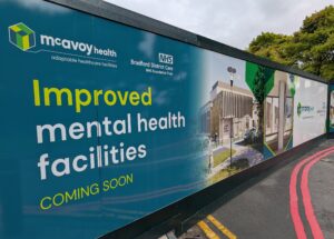 Image of hoarding around the LMH site that reads "improved mental health facilities coming soon"